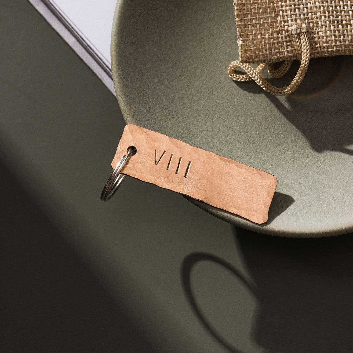 A keyring made from bronze that has been planished and engraved with the roman number symbols VIII which is the symbol for the number 8. The bronze keyring is on a moss green surface. The keyring is made by Empire Copper.